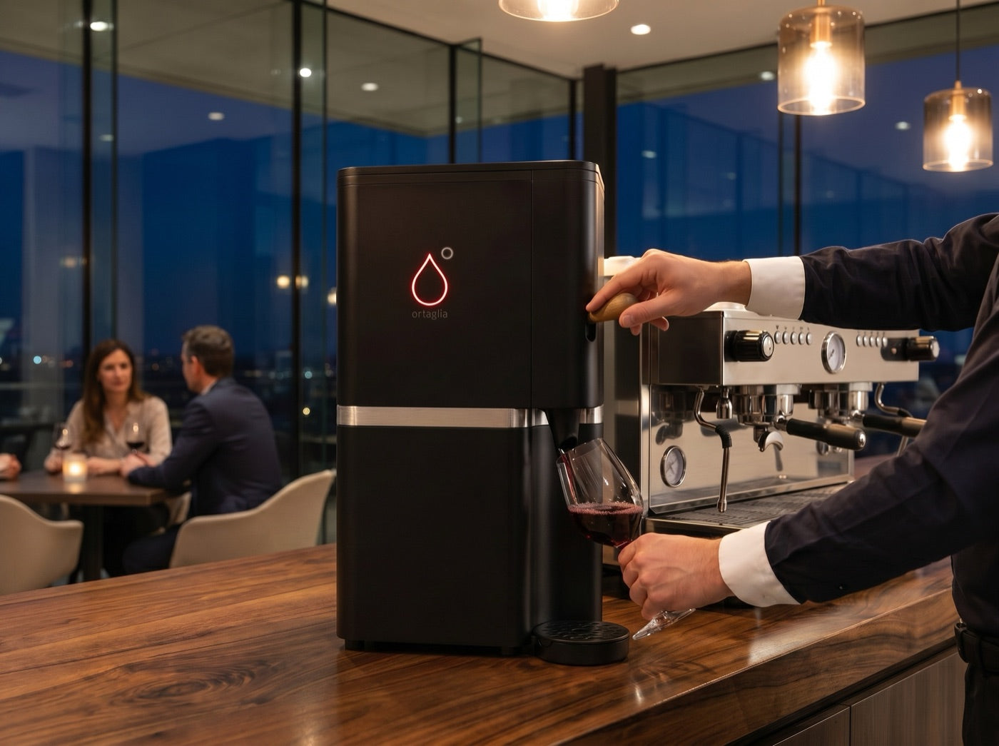 ortaglia Classic auf der Holztheke einer Bar am Abend – ein Glas Rotwein wird gezapft, im Hintergrund ein Paar bei Wein